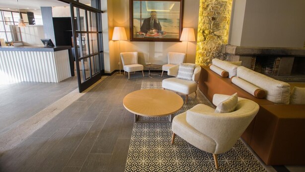 A modern hotel lobby with a reception desk, seating area with sofas and armchairs, a patterned rug, and a fireplace. - Hotel Brazv O (Vila do Conde)
