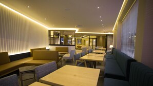 A modern dining area with multiple seating options including sofas and tables, and a large window providing natural light. - Hotel Brazv O (Vila do Conde)