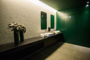 A modern bathroom with a textured wall, a long counter, two sinks, a mirror, and a green door. - Hotel Brazv O (Vila do Conde)