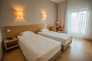A hotel room with two single beds, a wooden headboard, a nightstand with a phone, and a desk with a lamp. - Hotel Brazv O (Vila do Conde)