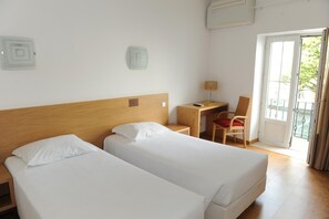 A hotel room with two single beds, a desk with a chair, and a window with a view of greenery. - Hotel Brazv O (Vila do Conde)