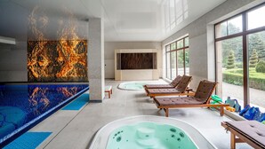 Zona de spa con hidromasaje, sillas de descanso y un amplio ventanal con vistas a un jardín.