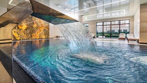 Una piscina interior con una cascada, ventanas amplias y un diseño de interiores moderno.