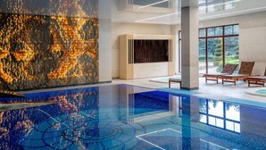 Un área de piscina interior moderna con piso reflectante, sillones de descanso y una pared grande con textura.