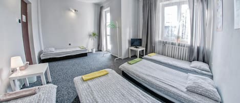 A hotel room with two single beds, a desk with a chair, a television, and a window with curtains.