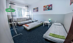 A room with two single beds, a desk, a chair, a radiator, and a window with curtains. - Place4us (Warsaw)