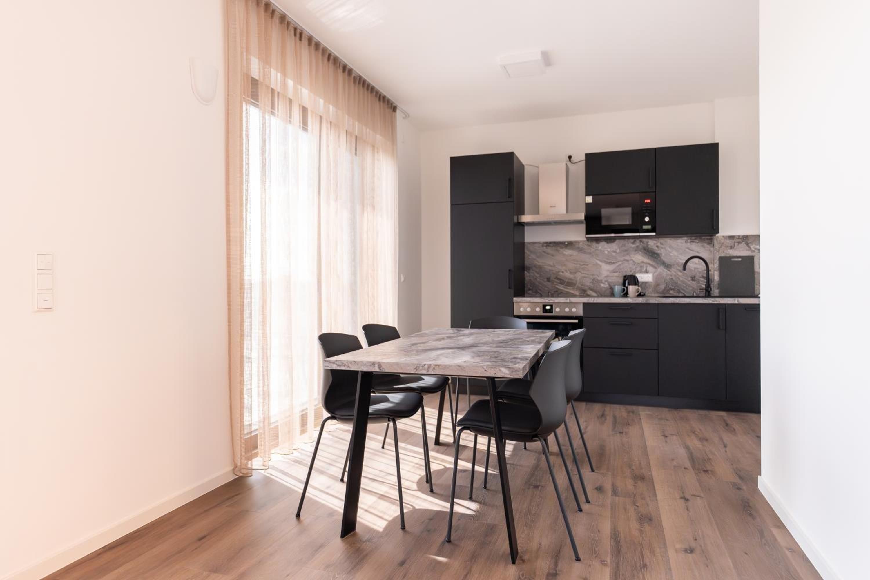 Une cuisine moderne avec un coin repas, comprenant un plan de travail en marbre, des meubles de rangement noirs et une table à manger avec des chaises.