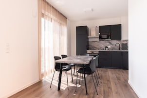 Una cocina moderna con comedor, que cuenta con encimera de mármol, armarios negros y una mesa con sillas.