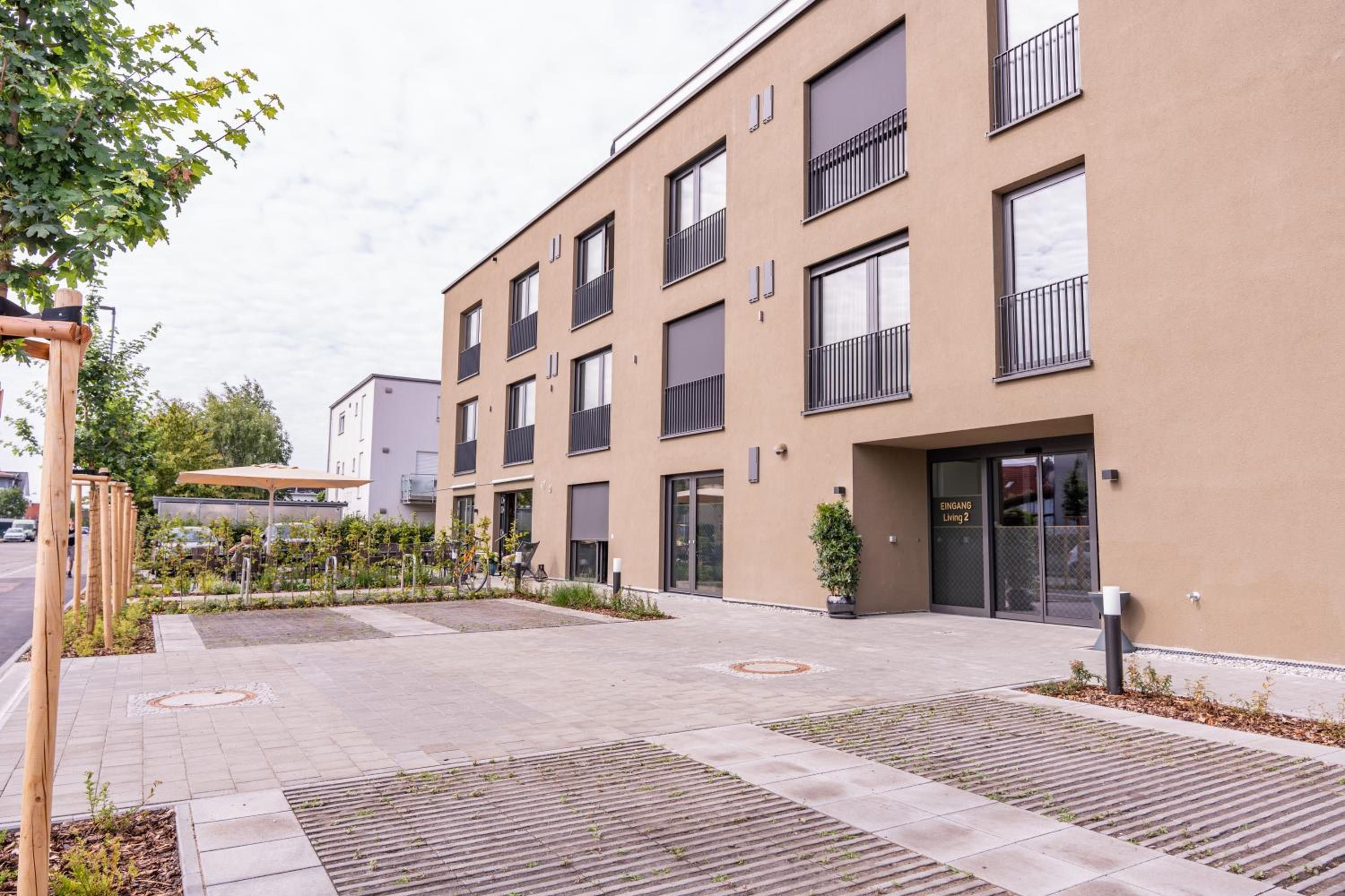 Un immeuble résidentiel moderne à plusieurs étages, doté de balcons, d’un espace extérieur aménagé et couvert, et d’une entrée sécurisée.