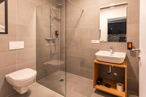 A modern bathroom with a glass-enclosed shower, a white toilet, and a wooden vanity with a sink. - Living Neuburg (Neuburg)