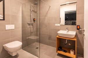 Um banheiro moderno com chuveiro em gabinete de vidro, vaso sanitário branco e toucador de madeira com pia.