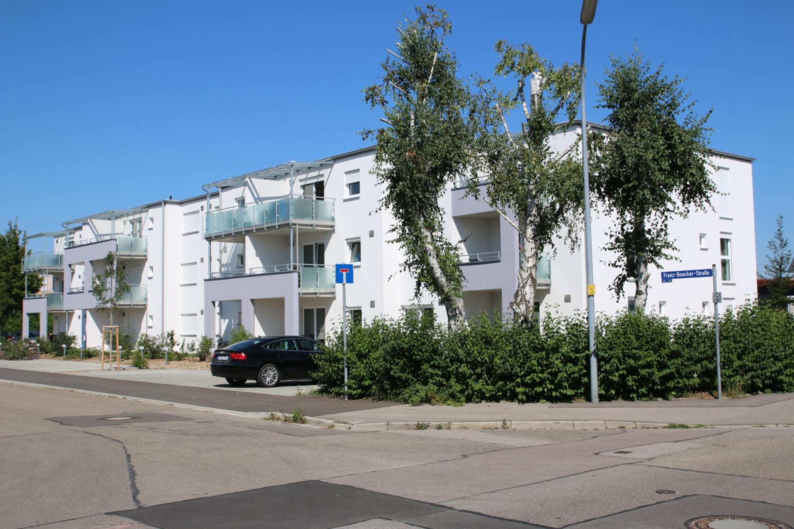 Un immeuble d’appartements moderne doté de balcons, une rue devant et une voiture garée sur le côté.