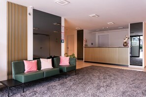 Un área de recepción moderna con un sofá verde, un panel de pared de madera y una mesa de recepción.