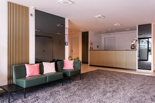 Uma área de recepção moderna com um sofá verde, parede revestida de madeira e um balcão de atendimento.