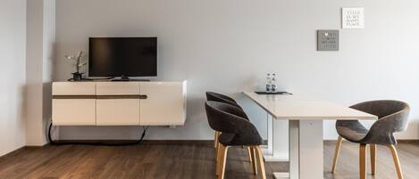 Un salon moderne avec un téléviseur à écran plat posé sur un meuble blanc, une table à manger avec quatre chaises et deux citations encadrées accrochées au mur.