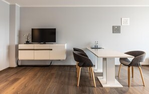 A modern living room with a flat-screen TV on a white cabinet, a dining table with four chairs, and two framed quotes on the wall. - Living Neuburg (Neuburg)