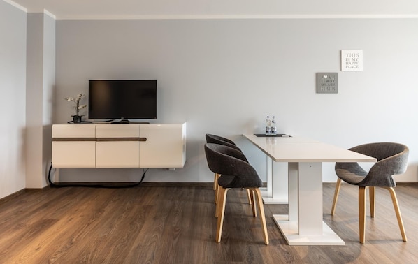 A modern living room with a flat-screen TV on a white cabinet, a dining table with four chairs, and two framed quotes on the wall. - Living Neuburg (Neuburg)