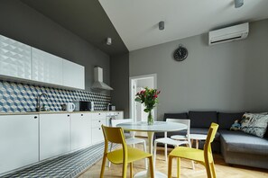 Une cuisine moderne avec des meubles blancs, un mur gris et un coin repas avec des chaises jaunes et une table blanche.