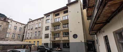 Um edifício residencial de vários andares, com varandas, área de estacionamento e uma grua de construção ao fundo.