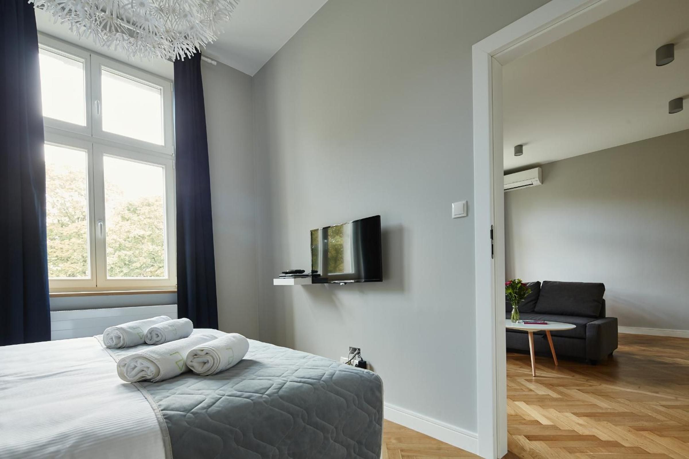 Una habitación de hotel moderna con una cama, un televisor de pantalla plana montado en la pared, una pequeña mesa con un florero y un sofá en la habitación contigua.