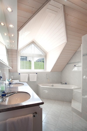 A modern bathroom with a skylight, a bathtub, and a vanity with a sink. - Seehotel Delphin (Meisterschwanden)