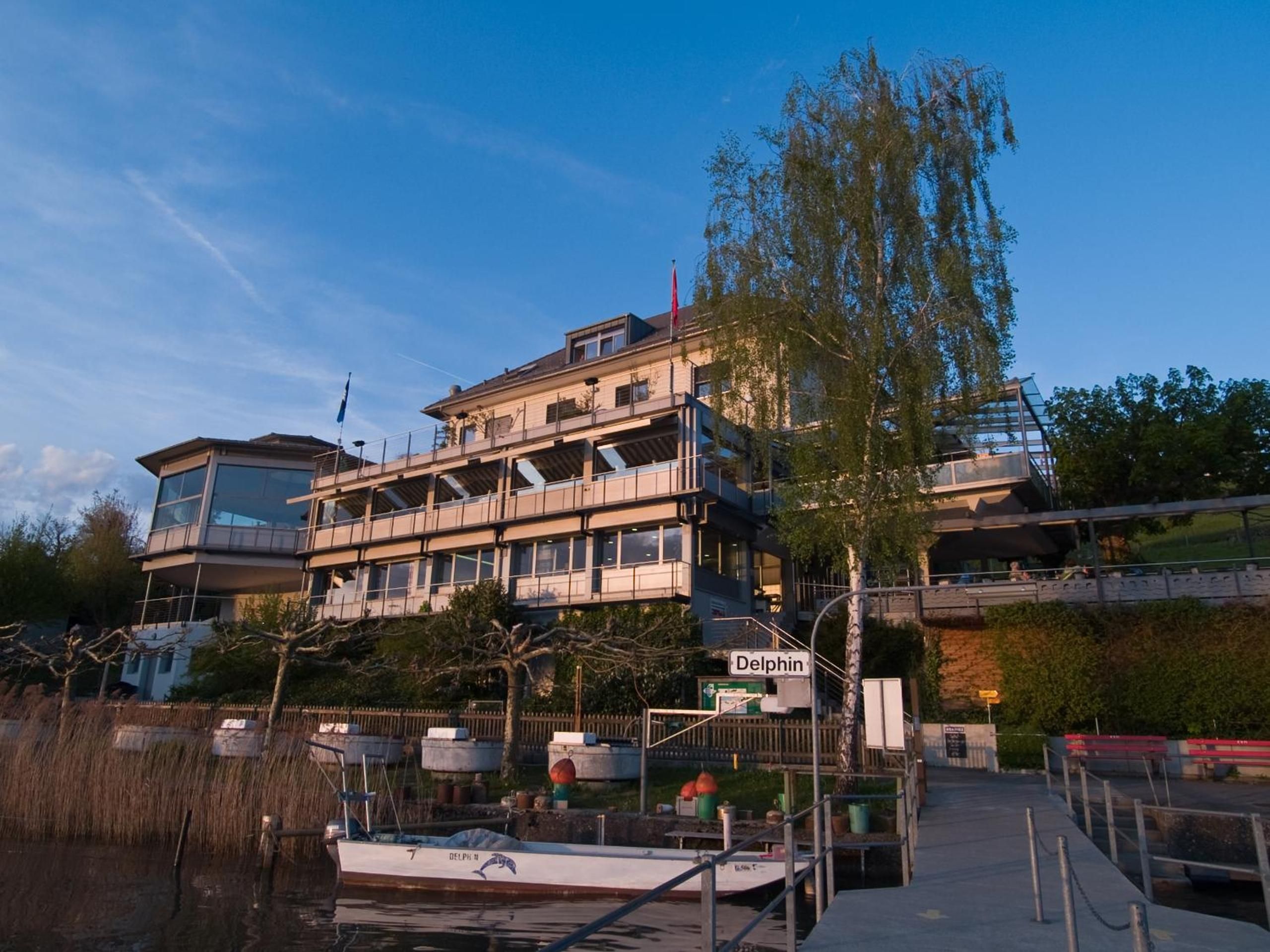 A multi-story building with a dock and a boat named 'Delphin' in the foreground.