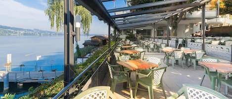 An outdoor terrace with tables and chairs, overlooking a body of water.