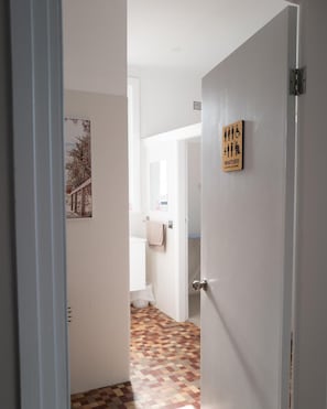 A hallway with a patterned floor, a door with a handwashing sign, and a partial view of a bathroom. - Seven Seas Hotel (Newcastle)
