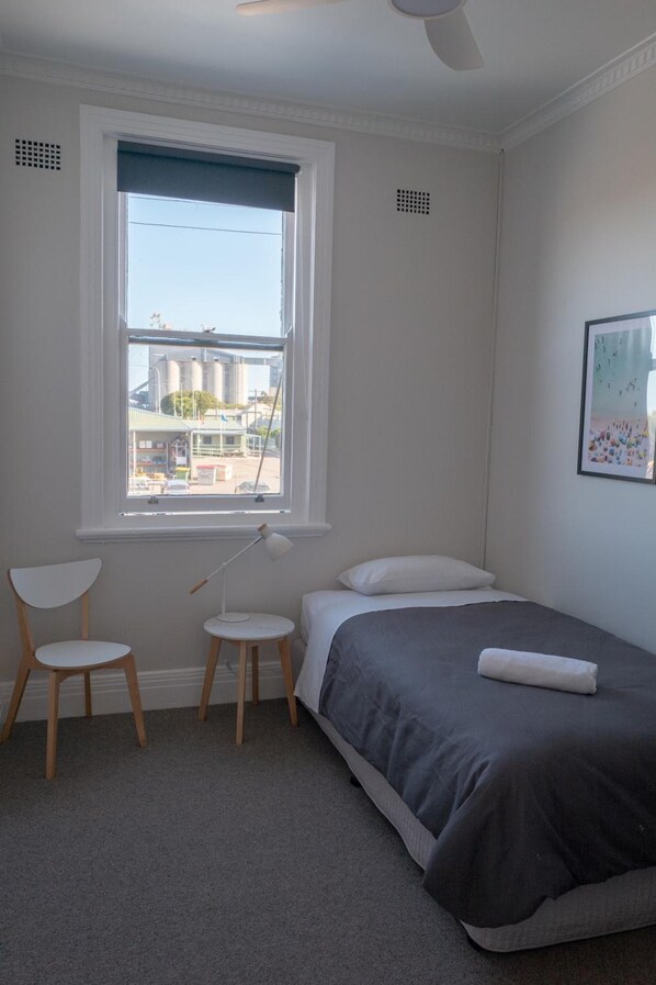 A bedroom with a bed, a chair, a small table, and a window with a view of industrial buildings. - Seven Seas Hotel (Newcastle)