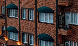 Un edificio de varios pisos de ladrillo con diseños de ventanas uniformes, incluyendo toldos y un balcón en el lado derecho.