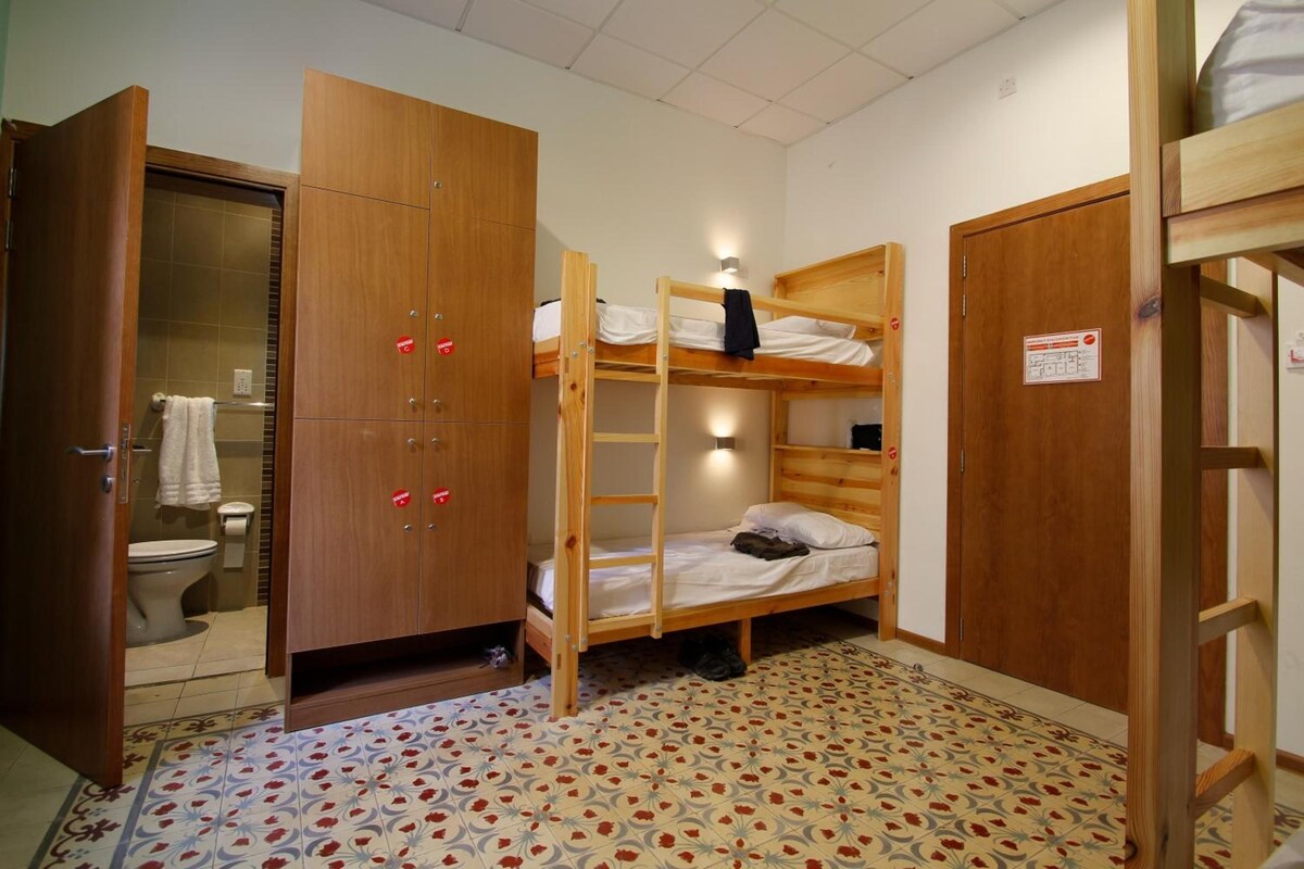 A small, compact room with a bunk bed, a wooden wardrobe, and a bathroom with a toilet and towel rack.