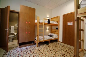 A small, compact room with a bunk bed, a wooden wardrobe, and a bathroom with a toilet and towel rack. - Corner Hostel (Sliema)