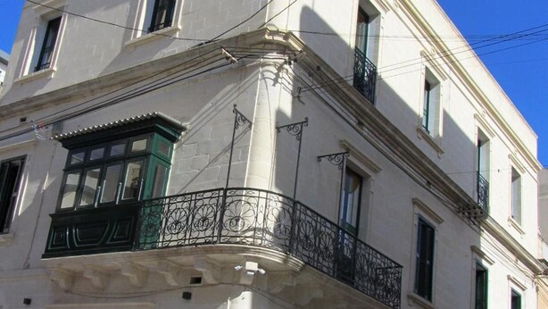 A multi-story building with a white facade, a balcony with a black wrought iron railing, and a red 'no entry' sign on the street. - Corner Hostel (Sliema)