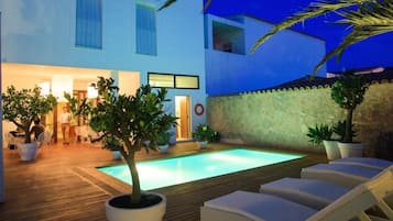 A poolside area with lounge chairs, a wooden deck, and potted plants.