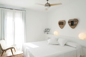 A bedroom with a bed, a chair, a ceiling fan, and two heart-shaped wall decorations. - Hotel Es Marv S (Formentera)