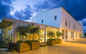 A two-story building with a cafe area in front, featuring outdoor seating and planters. - Hotel Es Marv S (Formentera)