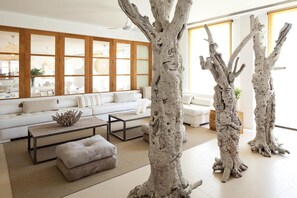 A modern living room with a white sofa, a coffee table, and two large tree sculptures. - Hotel Es Marv S (Formentera)