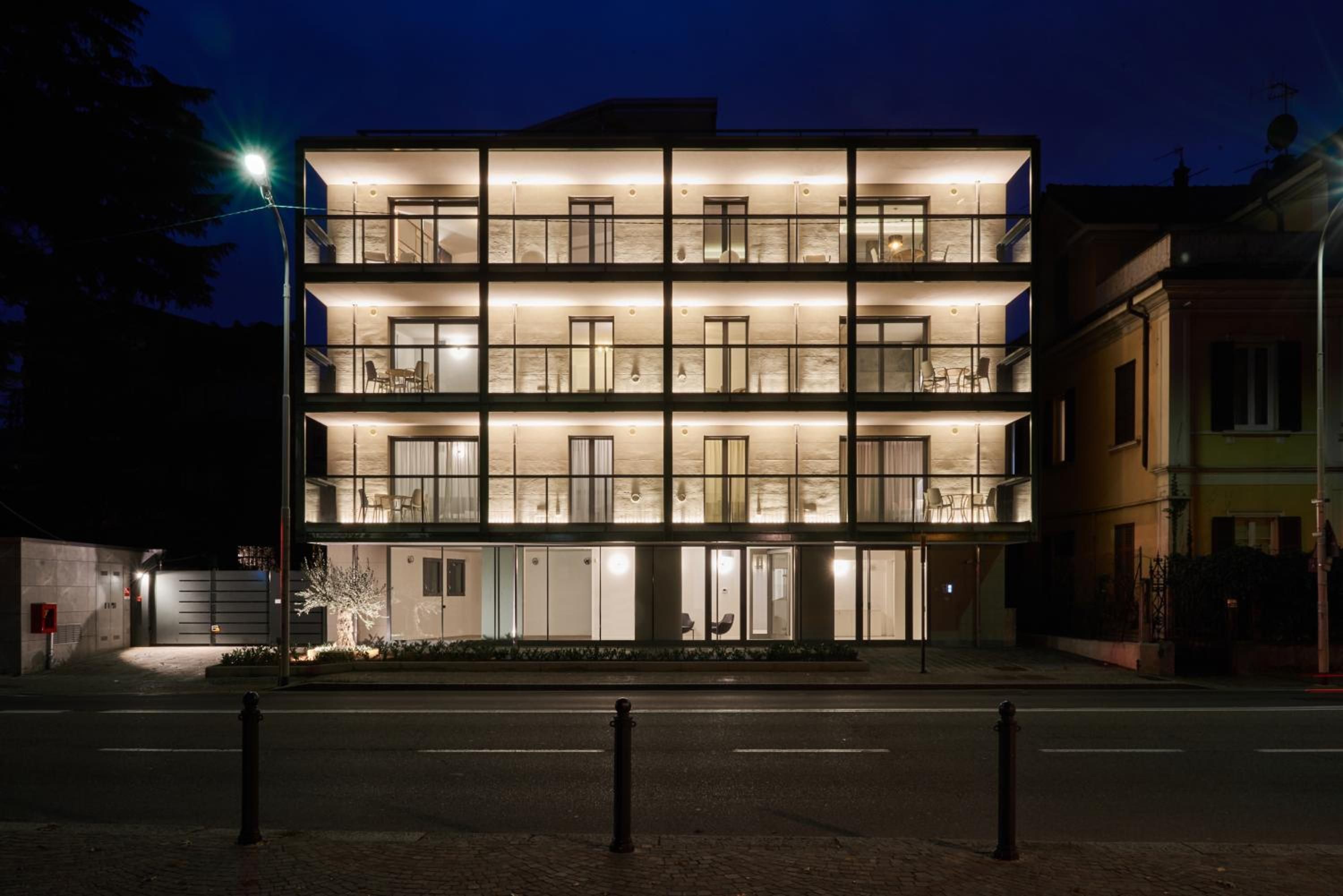 A multi-story hotel with a modern design, featuring balconies on each floor and a well-lit facade.