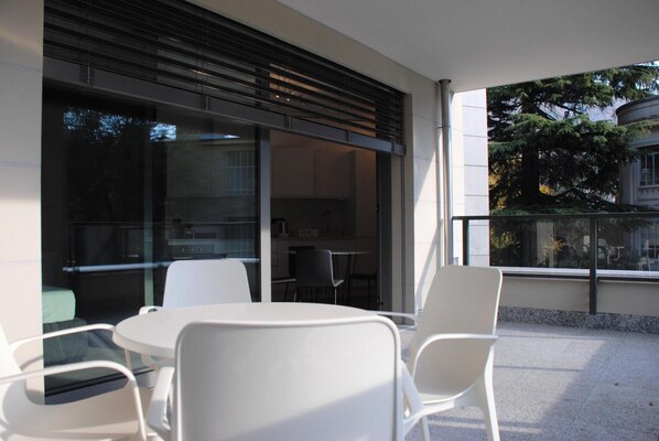 A modern outdoor seating area with a table and chairs, a sliding glass door leading to a kitchen, and a view of trees and buildings. - La Perla By Sedar (Como)