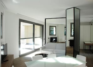 A modern living room with a white sofa, a glass coffee table, and a flat-screen TV. - La Perla By Sedar (Como)