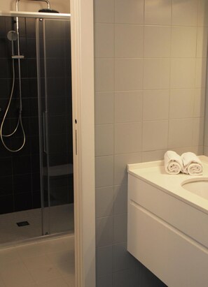 A bathroom with a glass-enclosed shower, a white sink, and a towel rack with towels. - La Perla By Sedar (Como)