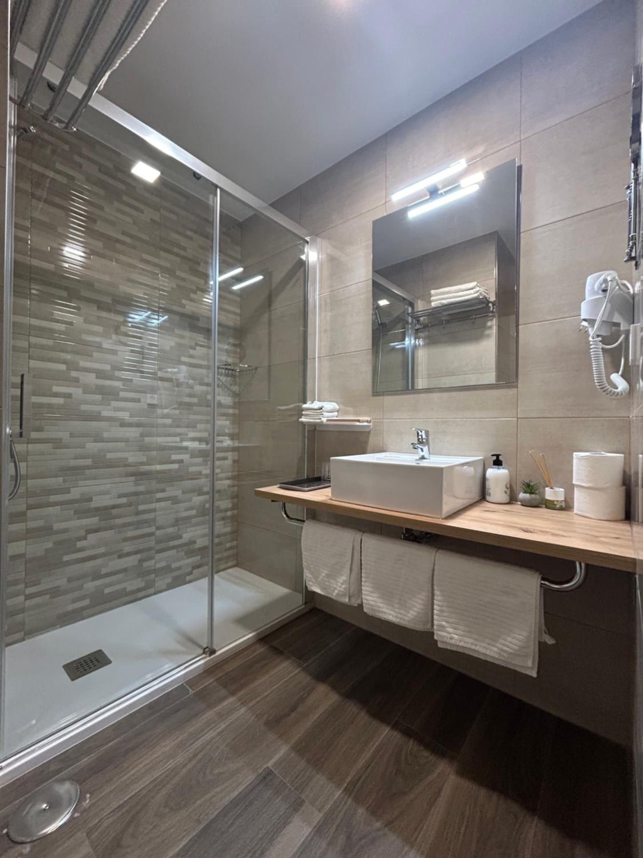 Un baño moderno con cabina de ducha de vidrio, tocador de madera, un espejo grande y teléfono incorporado.