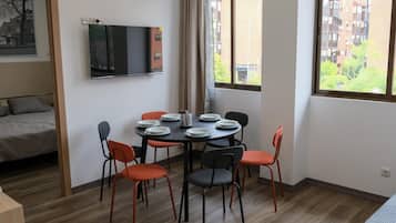 Una habitación con cama, una mesa de comedor con sillas, un televisor de pantalla plana montado en la pared y una ventana con vistas a edificios.