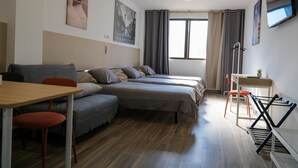 Quarto de hotel moderno com sofá, duas camas de solteiro, escrivaninha e televisão.