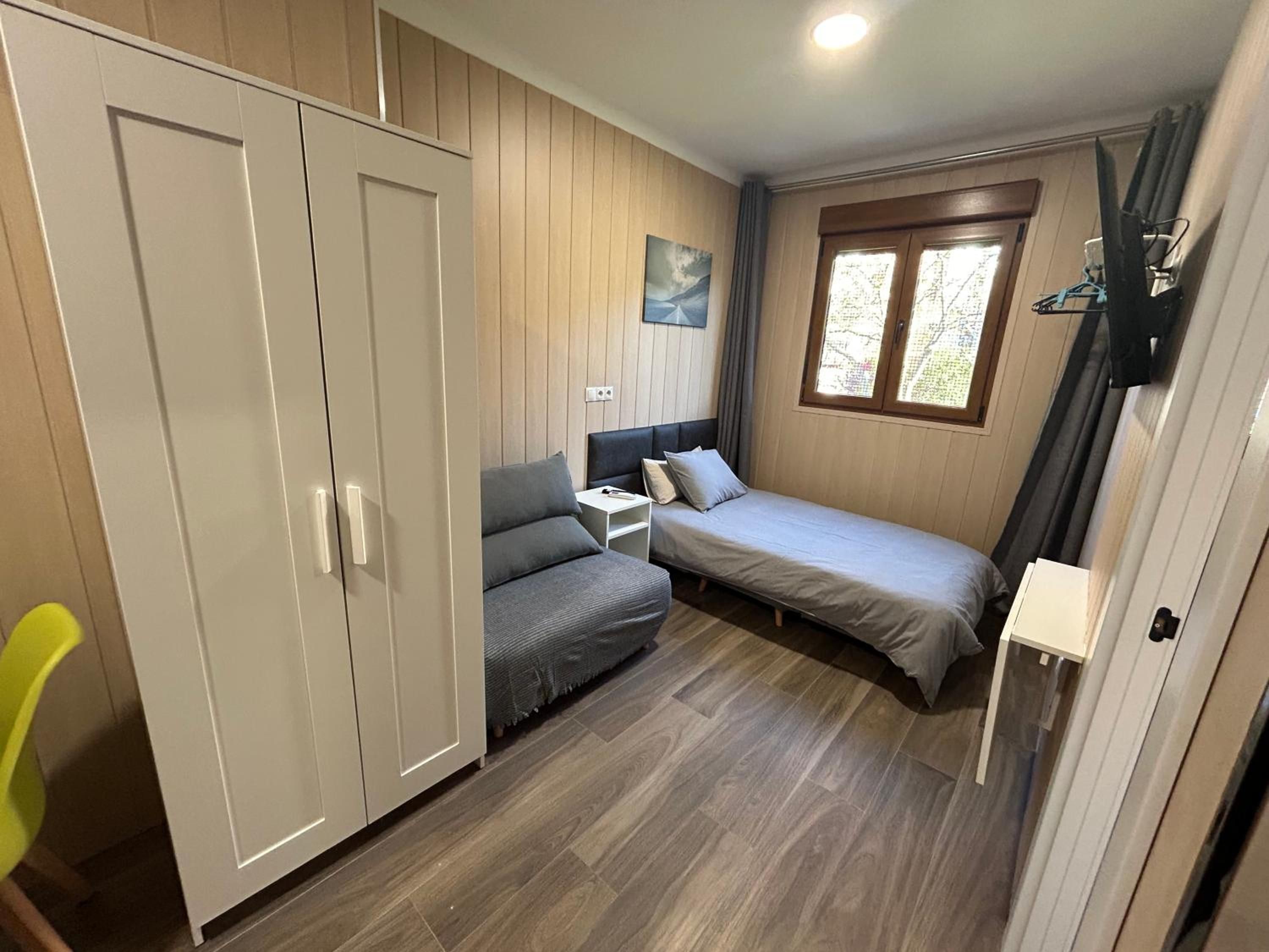 A compact room with a bed, a sofa, a wardrobe, and a window.