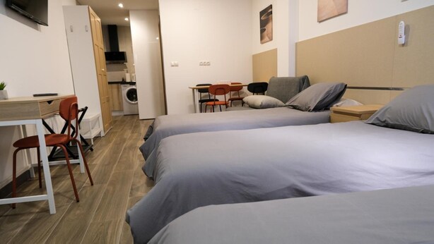 Quarto de hotel com duas camas, uma mesa, uma cadeira e uma kitchenette.