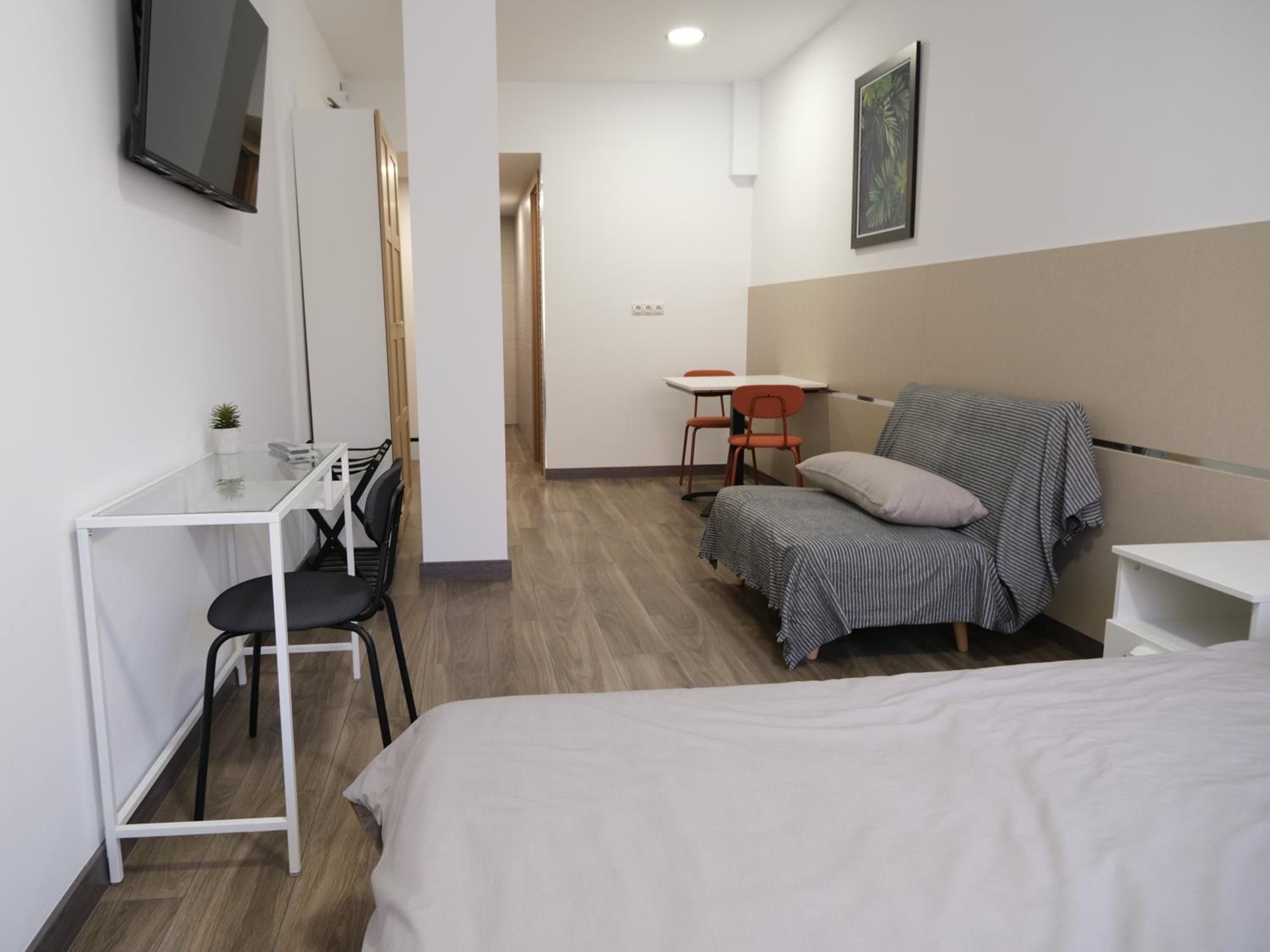 A hotel room with a bed, a desk with a chair, a small table with two chairs, and a TV mounted on the wall.