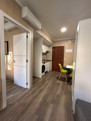 A compact kitchen with a washing machine, a dining area with a table and chairs, and a wooden floor. - Alianza Suites (Madrid)