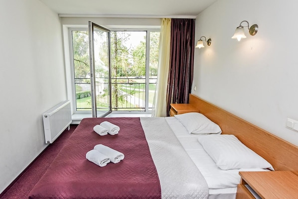A hotel room with a bed, a window with a view of the outdoors, and a nightstand. - Muza Hotel (Palanga)