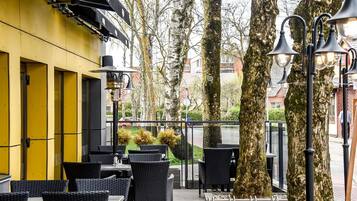 Un espacio al aire libre con mesas y sillas de mimbre, un edificio amarillo y árboles.
